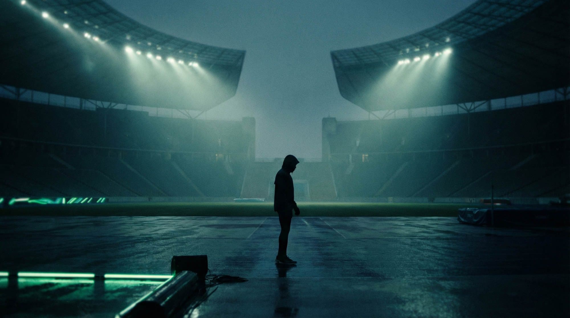 Lone athlete standing on a rain-soaked pitch under stadium floodlights