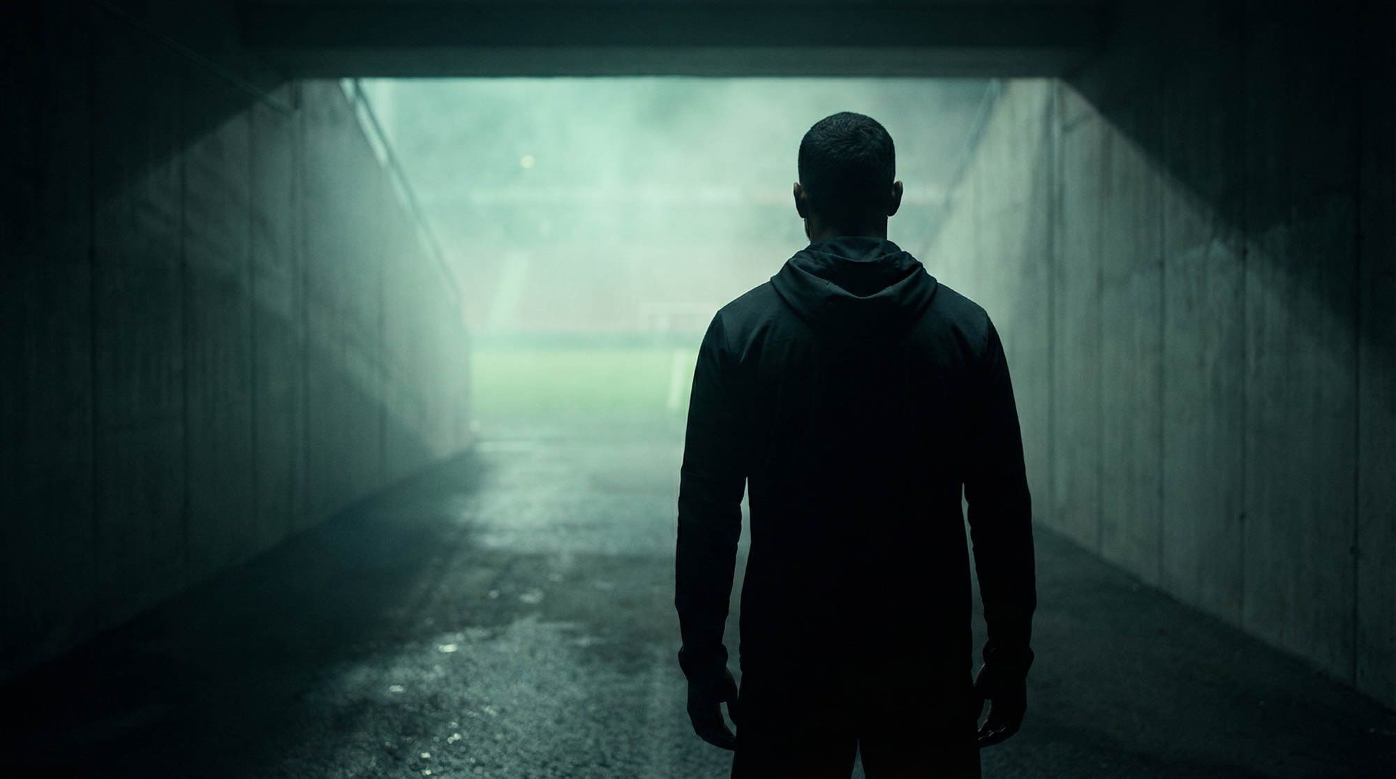 Athlete in a hooded top walking through a dark stadium tunnel